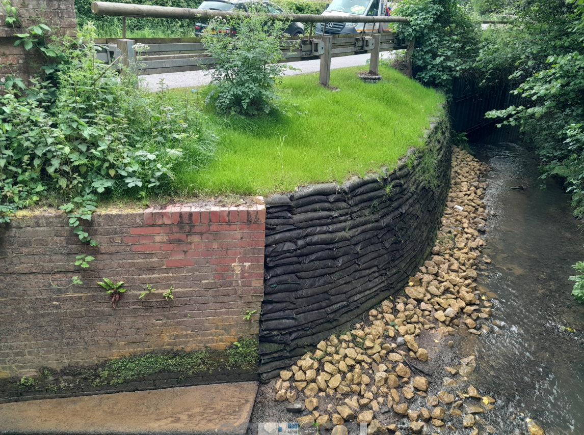 Image of a retaining wall next to a stream, made from bags of soil and seed.
